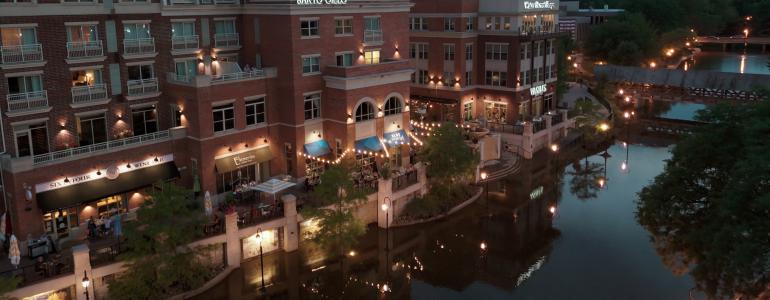 Riverside buildings at dusk with lit pathways and reflections on the water.