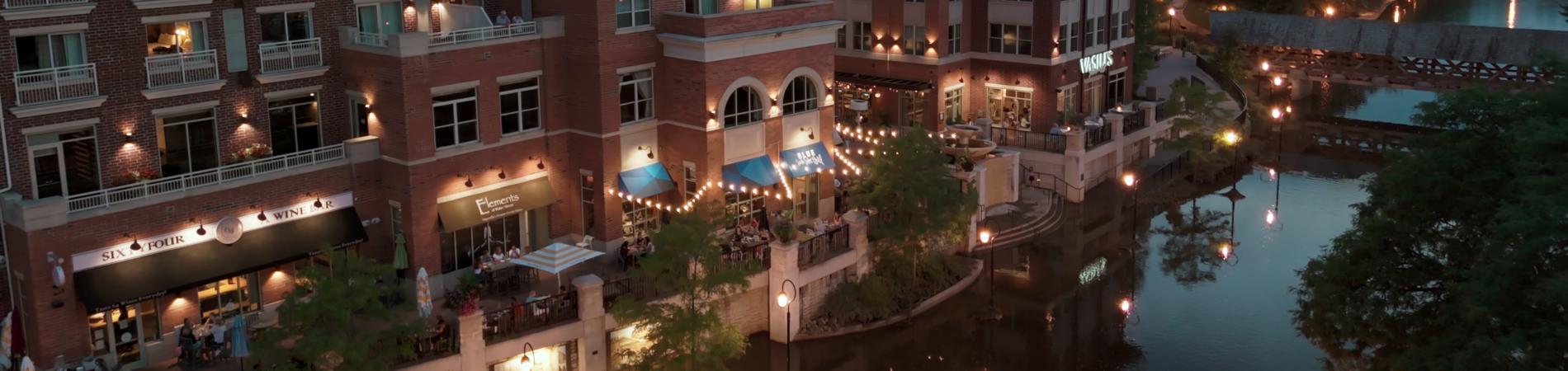 Riverside buildings at dusk with lit pathways and reflections on the water.